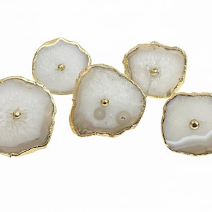 Puede incluir: Cinco tiradores decorativos para armarios con diseño de ágata natural. Cada tirador presenta una rebanada de ágata blanca y gris con un borde dorado y un pequeño tornillo dorado en el centro. Estos tiradores son ideales para añadir un toque de elegancia natural.