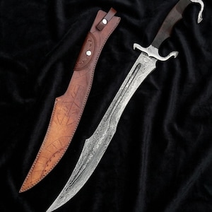 May include: A detailed image of a decorative dagger with a curved blade and a dark wooden handle. The blade has an intricate pattern, and the handle features a curved design. A brown leather sheath with embossed patterns accompanies the dagger. The dagger and sheath are displayed on a black surface.