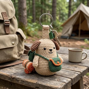 May include: A crocheted dog keychain with brown ears and a green and orange backpack and satchel. The dog is attached to a silver keyring with keys. A tan backpack, a mug, and a rolled-up blanket are also visible.