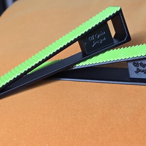 May include: Two black and green push-up blocks with a textured green top and the text "Ed Gode Designs". The blocks are angled and designed for push-up exercises. The blocks are on an orange surface.