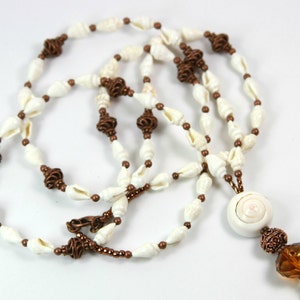 May include: A handmade lanyard featuring white seashells, copper-coloured wire accents, and small brown beads. The lanyard includes a large, round shell pendant and a copper-coloured clasp. The design is suitable for holding keys or an ID badge.