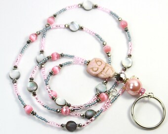 May include: A beaded lanyard featuring pink, gray, and iridescent beads. The lanyard has a pink owl pendant and a large pink pearl with a silver key ring. The beads are strung on a thin, flexible cord.