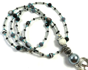 May include: A beaded lanyard featuring a variety of beads in black, gray, and white. The lanyard includes a white owl bead, a large gray pearl, and a silver-colored clasp. The beads are strung on a silver-colored wire.