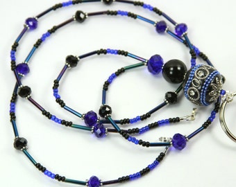 May include: A beaded lanyard with a mix of black, blue, and iridescent beads. The lanyard features faceted blue crystals, black faceted beads, and a decorative black and silver bead with blue accents. A silver key ring is attached.
