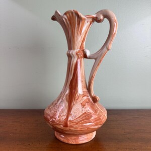May include: A decorative ceramic pitcher with a marbled design in shades of brown and white. The pitcher has a flared top, a curved handle, and a rounded base. The pitcher is approximately 8 inches tall.