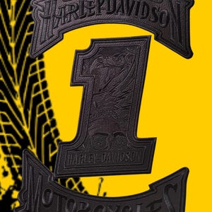 Op de afbeelding: Een zwarte geborduurde embleemset met een groot cijfer één met een schedelafbeelding, bekroond met een Harley-Davidson-boog en een onderste banner met de tekst Motorcycles, tegen een felgele achtergrond met zwarte bandensporen.