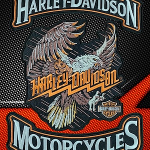 Puede incluir: Un conjunto de tres parches bordados que presenta un gráfico central de un águila con el texto Harley-Davidson en naranja, flanqueado por parches superiores e inferiores que dicen Harley-Davidson y Motorcycles en letras blancas con bordes naranjas.