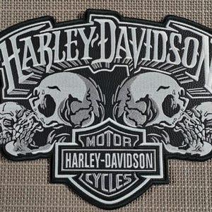 Puede incluir: Parche Harley-Davidson en blanco y negro con el nombre de la marca y "MOTOR CYCLES". El parche tiene un diseño de calavera con fondo negro y costuras blancas. El parche es un emblema.