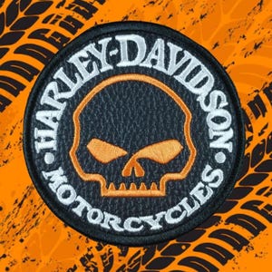 Puede incluir: Un parche redondo de Harley-Davidson Motorcycles con un diseño de calavera. El parche presenta un fondo negro con un contorno de calavera naranja y texto blanco. El texto dice "HARLEY-DAVIDSON MOTORCYCLES".