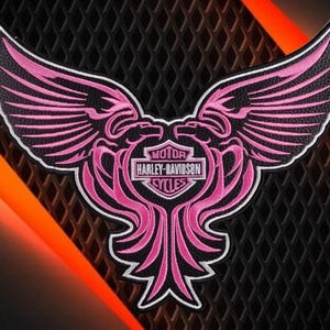 Puede incluir: Un parche bordado en negro y rosa que presenta un águila estilizada con las alas extendidas. En el centro, un emblema en forma de escudo muestra el texto MOTOR HARLEY-DAVIDSON CYCLES. El diseño está delineado con hilo blanco sobre fondo negro.
