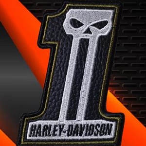 Op de afbeelding: Een zwart-witte geborduurde patch in de vorm van het cijfer één, met een gestileerd schedelontwerp aan de bovenkant en de tekst Harley-Davidson aan de onderkant. De patch heeft een zwarte textuurachtergrond met wit stiksel en een dunne gouden rand.