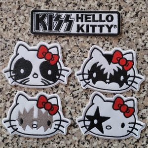 Puede incluir: Parches bordados que combinan KISS y Hello Kitty. Los parches presentan el logotipo de KISS y caras de Hello Kitty con maquillaje inspirado en KISS. Los parches son blancos, negros, rojos y grises.