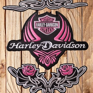 Puede incluir: Conjunto de parches Harley-Davidson en negro, rosa y blanco. El parche central presenta el logotipo de Harley-Davidson con detalles en rosa. Parches adicionales incluyen diseños florales y de desplazamiento decorativos, todos bordados.