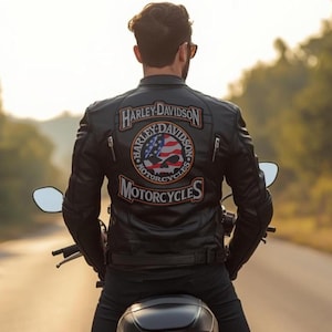 Könnte beinhalten: Eine schwarze Motorradjacke aus Leder mit einem großen Rückenaufnäher, der den Schriftzug Harley-Davidson Motorcycles sowie ein zentrales Totenkopf-Motiv mit US-Flaggenmuster und orange-weißen Stickereidetails aufweist.