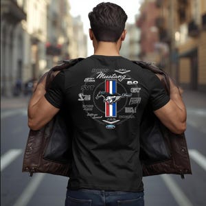 May include: Black t-shirt with a Mustang logo, red, white, and blue stripes, and a running horse graphic. The shirt has text including "BOSS 302", "SVT", and "Mach 1". The shirt is being worn.