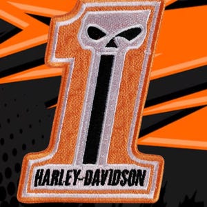 Puede incluir: Parche bordado naranja con el número "1", un diseño de calavera y el texto "HARLEY-DAVIDSON". El parche tiene un borde blanco y está sobre un fondo negro y naranja.