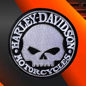 Puede incluir: Un parche bordado circular que presenta un gráfico de calavera blanca centrado dentro de un borde negro. El texto "HARLEY-DAVIDSON" está arqueado en la parte superior y "MOTORCYCLES" en la parte inferior en letras mayúsculas blancas.