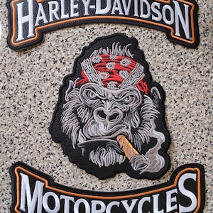 Op de afbeelding: Een driedelige set geborduurde patches met een bovenste boog met witte Harley-Davidson tekst, een onderste boog met witte Motorcycles tekst en een centrale patch met een grijze gorilla die een rode bandana draagt en een sigaar rookt.