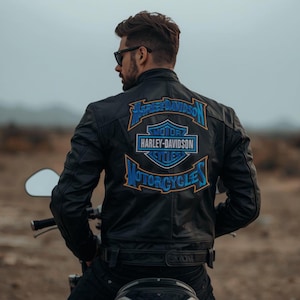 May include: Black leather motorcycle jacket with the Harley-Davidson logo in blue and white on the back. The jacket has a classic biker style with a stand-up collar and zippered pockets. The image shows the back of the jacket.
