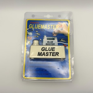 May include: A Jobar's Glue Master hot glue pot in its original clear plastic blister packaging. The white rectangular device features the text Glue Master on the front. The blue cardboard backing displays product features and a hand illustration.