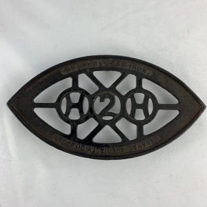 May include: Antique cast iron Humphrey Gas Iron. The oval-shaped iron features an openwork design with the letters "H2H" in the center. The text "HUMPHREY GAS IRON" and "GENERAL SPECIALTY CO." are visible on the iron.