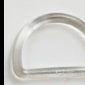 May include: A clear, D-shaped plastic ring. The ring is semi-circular with a flat bottom and a small marking on the flat edge. The ring is made of a transparent material and is set against a white background.