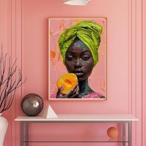 Könnte beinhalten: Gerahmtes Ölgemälde einer schwarzen Frau mit grünem Kopftuch, die eine Pfirsich hält. Das Kunstwerk steht auf einem weißen Tisch mit Metallrahmen vor einer rosa Wand. Eine weiße Vase mit schwarzen Zweigen und eine geometrische Pendelleuchte sind ebenfalls zu sehen.