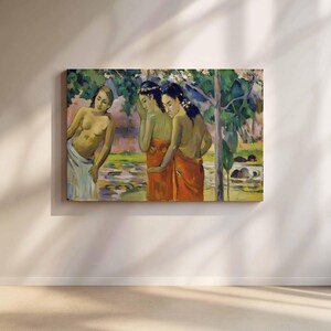 Puede incluir: Una impresión enmarcada de una pintura que representa a tres mujeres en un entorno tropical. Dos mujeres llevan enaguas naranjas, mientras que la tercera lleva una enagua blanca. El fondo presenta exuberante vegetación y una masa de agua, con un cielo rosa y verde.