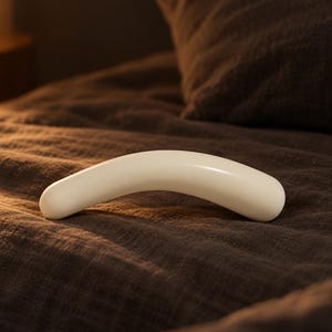 May include: A smooth, curved, off-white object with a rounded, elongated shape. The surface is solid and matte, featuring a gentle arch that tapers slightly at both ends. The object is positioned horizontally, showcasing its clean, simple, and continuous form.