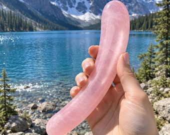 May include: A smooth, curved, cylindrical object carved from translucent light pink rose quartz. The stone has a polished, glossy finish with subtle internal variations in color and texture, featuring a rounded tip and a slightly tapered base.