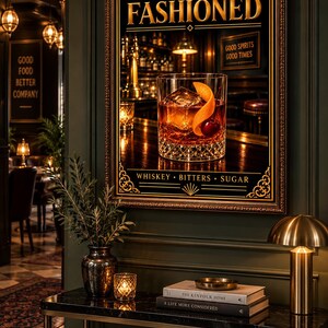 K&ouml;nnte beinhalten: Ein gerahmter Wandkunstdruck mit dem Titel OLD FASHIONED, der ein Glas Whiskey mit Eis, einer Orangenschale und einer Kirsche zeigt. Der Text lautet WHISKEY BITTERS SUGAR. Der Druck h&auml;ngt &uuml;ber einem Konsolentisch mit B&uuml;chern und einer Lampe.
