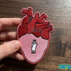 May include: A rustic wooden sign with the text "Welcome" in a handwritten style. The sign is painted white with a distressed finish, and features a decorative floral element in the corner. The background is a blurred image of a home.