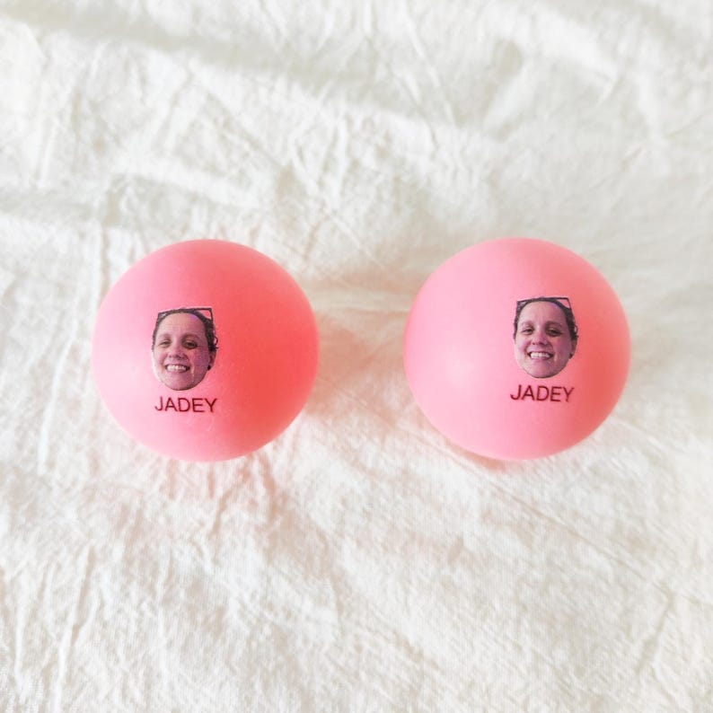 May include: Two round, bright pink stress balls, each featuring a small, centered photographic print of a smiling person's face above the printed name JADEY in black capital letters. The surface of the balls is smooth and matte.