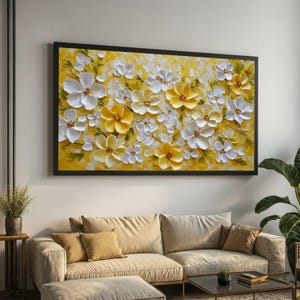 May include: A framed floral artwork depicting white and yellow flowers with green foliage on a yellow backdrop. The painting, in a black frame, hangs above a beige sofa, offering a nature-inspired decorative element.