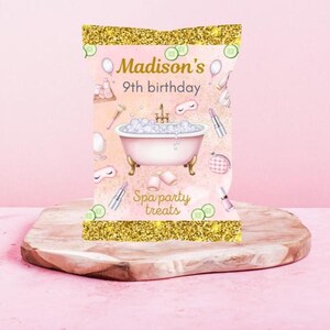 May include: A pink and gold party favor bag with the text "Madison's 9th birthday" and "Spa party treats." The bag features illustrations of spa-related items, including a bathtub, makeup, and cucumbers.