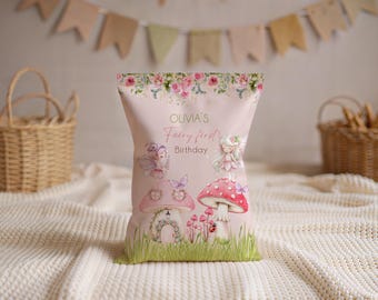 May include: A pink party favor bag with a fairy theme. The bag features illustrations of fairies, mushrooms, and butterflies. Text on the bag reads "Olivia's Fairy first Birthday". The top of the bag is decorated with a floral design.