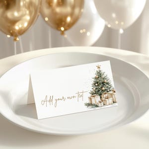 Peut inclure: Carte pliée blanche avec une illustration à l'aquarelle d'un sapin de Noël et de cadeaux. Le texte "Add your own text" est en or. Des ballons dorés et blancs sont en arrière-plan.