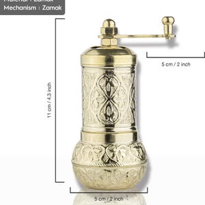 May include: A gold-colored pepper grinder made of Zamak. The grinder is 4.3 inches tall and 2 inches wide, featuring an ornate floral pattern. It has a hand crank and a Zamak mechanism.