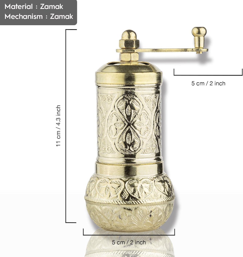May include: A gold-colored pepper grinder made of Zamak. The grinder is 4.3 inches tall and 2 inches wide, featuring an ornate floral pattern. It has a hand crank and a Zamak mechanism.