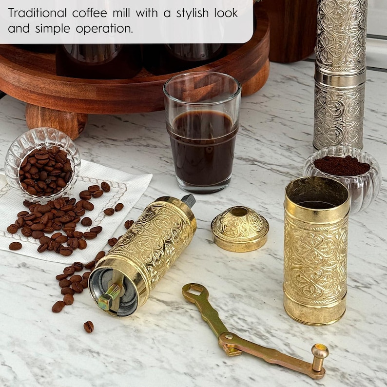 Pode incluir: Um moinho de caf&eacute; tradicional com um visual elegante e opera&ccedil;&atilde;o simples. A imagem mostra um moedor de caf&eacute; dourado com um design ornamentado, um copo de caf&eacute; e gr&atilde;os de caf&eacute;. O texto na imagem diz: "Moinho de caf&eacute; tradicional com um visual elegante e opera&ccedil;&atilde;o simples."