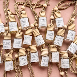 May include: A collection of small glass car air freshener bottles with light wood caps and hanging rope cords. Each bottle features a white label with the text Coal Candle Co. and various scent names like Brown Sugar & Banana and Pumpkin Souffle.