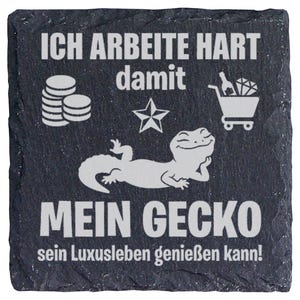 Könnte beinhalten: Ein quadratischer Untersetzer aus schwarzem Schiefer mit weißer Gravur, die den Text ICH ARBEITE HART damit MEIN GECKO sein Luxusleben genießen kann! zeigt. Das Design enthält Symbole für einen Münzstapel, einen Stern und einen Einkaufswagen.