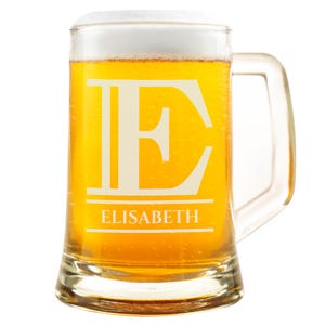Könnte beinhalten: Ein klares Bierkrug aus Glas, gefüllt mit goldenem Bier und bedeckt mit weißem Schaum. Der Krug zeigt einen großen weißen Buchstaben "E" und den Namen "ELISABETH" in weißer Schrift.