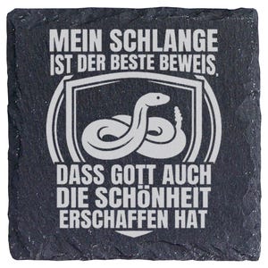 Könnte beinhalten: Ein quadratischer Untersetzer aus schwarzem Schiefer mit rauen, unebenen Kanten. Die Oberfläche zeigt eine weiße Gravur einer zusammengerollten Klapperschlange in einem Schild-Umriss sowie den Text: MEIN SCHLANGE IST DER BESTE BEWEIS, DASS GOTT AUCH DIE SCHÖNHEIT ERSCHAFFEN HAT.