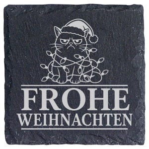 Könnte beinhalten: Ein quadratischer Untersetzer aus schwarzem Schiefer mit einer Gravur eines mürrischen Katzenmotivs, das eine Weihnachtsmütze trägt und in Lichterketten verwickelt ist. Darunter ist der Text FROHE WEIHNACHTEN in weißer, großgeschriebener Schrift eingraviert.