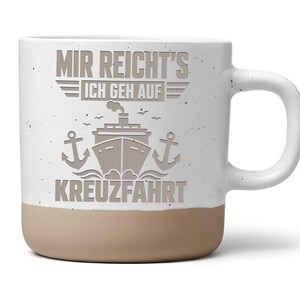 Könnte beinhalten: Ein weißer Keramikbecher mit Sprenkeloptik und einem beigefarbenen Boden. Auf der Vorderseite befindet sich eine graue Grafik eines Kreuzfahrtschiffes, flankiert von zwei Ankern, sowie der Text "MIR REICHT'S ICH GEH AUF KREUZFAHRT" in Blockschrift.