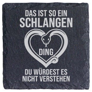 Könnte beinhalten: Ein quadratischer Untersetzer aus dunkelgrauem Schiefer mit einer weißen Gravur, die eine Schlange in Herzform zeigt. Der Text lautet: DAS IST SO EIN SCHLANGEN DING DU WÜRDEST ES NICHT VERSTEHEN. Der Untersetzer hat eine raue, strukturierte Kante.