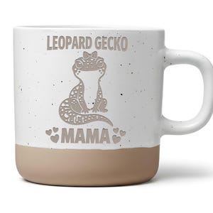 Könnte beinhalten: Ein weißer Keramikbecher mit gesprenkelter Oberfläche und einem beigen Boden. Auf der Vorderseite befindet sich eine braune Grafik eines Leopardengeckos mit einer kleinen Schleife, umgeben vom Schriftzug LEOPARD GECKO MAMA und kleinen Herzen.