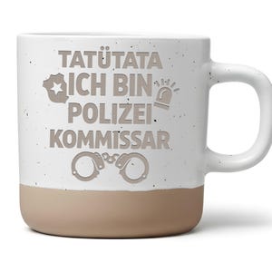 Könnte beinhalten: Ein weißer Keramikbecher mit gesprenkelter Oberfläche und beigem Boden. Auf der Vorderseite steht der Text TATÜTATA ICH BIN POLIZEI KOMMISSAR in Grau, ergänzt durch Symbole eines Polizeisterns, einer Sirene und einer Handschelle in der Mitte.