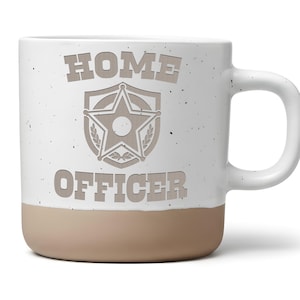 Könnte beinhalten: Ein weißer Keramikbecher mit gesprenkelter Oberfläche und beigem Boden. Auf der Vorderseite steht der Text "HOME OFFICER" in Blockschrift, zentriert über und unter einer Grafik eines fünfzackigen Sterns in einem Schildemblem mit Lorbeerblättern.